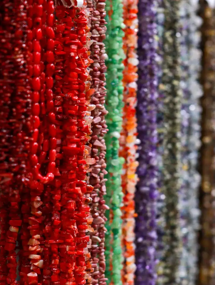 Fios de pedras naturais pendurados lado a lado na Kita Centro, em degradê do vermelho ao roxo