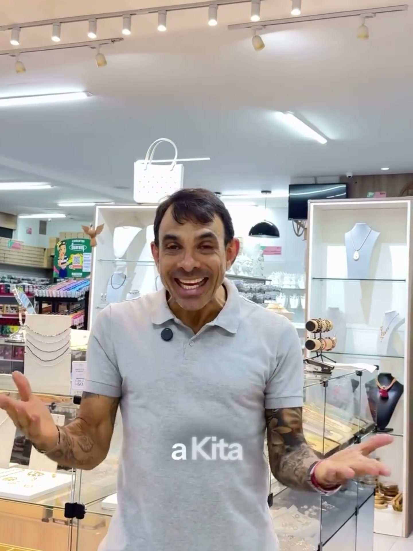 Raphael Tosto apresentando a loja, sorrindo, entre vitrines de bijuteria